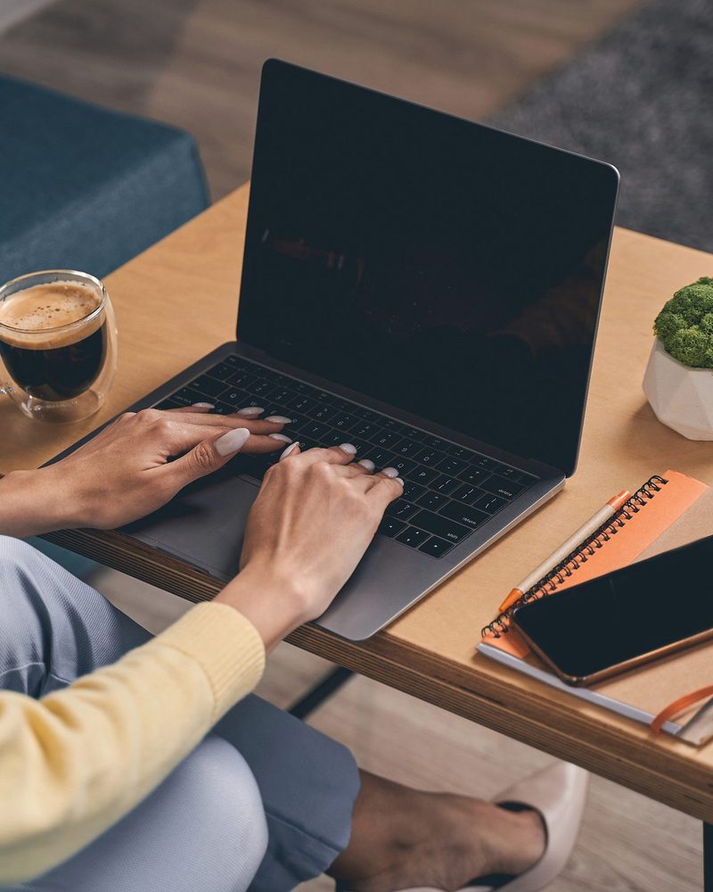 A teacher planning at a laptop with a notebook and a cup of coffee